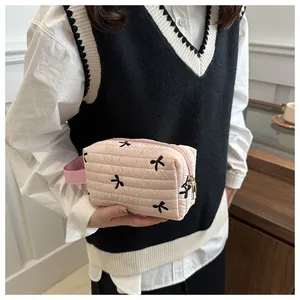 Close-up of pink quilted cosmetic bag with black bow embroidery and gold metal zipper