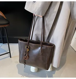 Detail of dark brown leather tote bag with subtle texture and round geometric pendant charm
