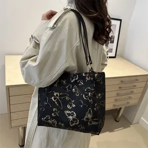 Large black shoulder tote bag featuring gold butterfly print and metallic ring buckles