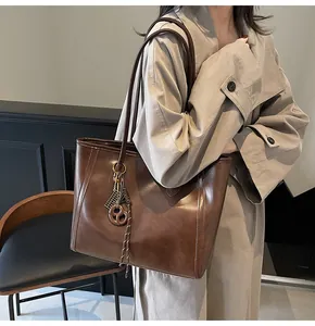 Brown leather tote bag side view on model featuring vintage stitching and bag charm