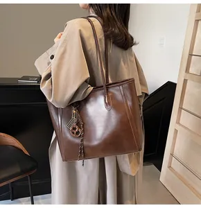 Detail of dark brown leather tote bag with braided knot and metallic pendant accessory