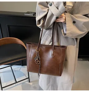 Detail view of dark brown faux leather tote bag with stylish charm on gray trench coat