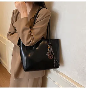Detail of minimalist black leather tote bag with decorative charm on camel blazer outfit