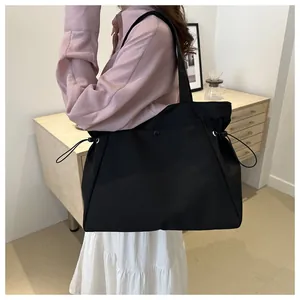 Detail of a large black nylon tote bag with side drawstring design shown on a shoulder