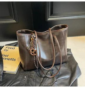 Macro shot of dark brown tote bag with decorative metal tags and knotted charm detail
