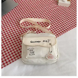 Détail du petit sac bandoulière en toile crème avec motif chien saucisse et pendentif