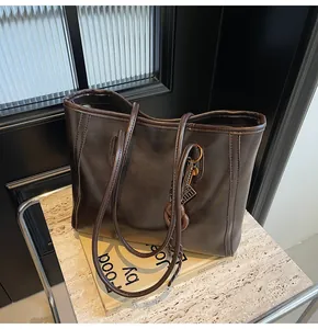 Detail of dark brown faux leather tote bag with vertical stitching and metal chain charm