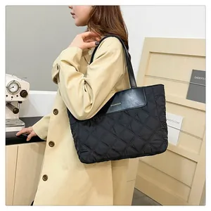 Detail of black quilted nylon tote bag featuring a leather patch with fashion lettering