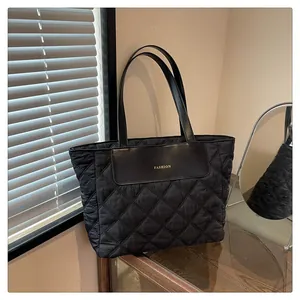 Detail of quilted black nylon tote bag showing gold FASHION text and vegan leather trim
