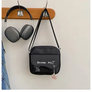 Détail du sac bandoulière en nylon noir avec motif de teckel et pendentif rose au crochet