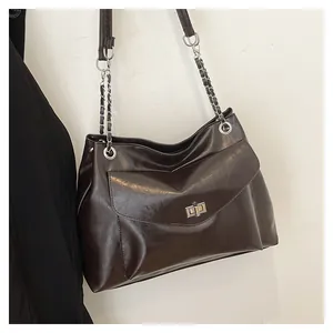 Detail of dark brown leather tote featuring a silver twist lock and metal chain strap