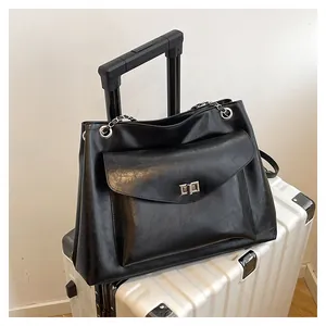 Detail of black leather tote bag with silver metal swivel lock on a white suitcase