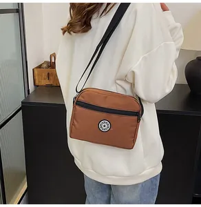 Detail view of a brown nylon crossbody bag with sport badge worn on a white sweater