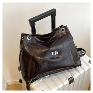 Detail of metal chain strap and flap pocket with turn-lock on coffee brown tote bag