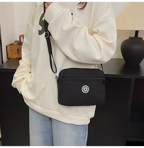 Close-up of lightweight black nylon crossbody bag featuring round sport logo and zipper