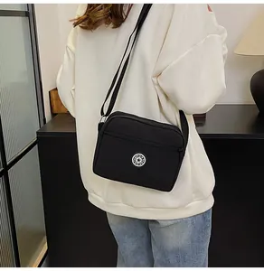 Detail of black oxford fabric crossbody bag showing the SPORT logo and zipper pockets