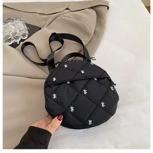 Detail view of black quilted mini round crossbody bag with white bow embroidery and strap