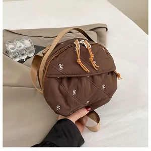 Close-up of brown circular quilted handbag with bow embroidery and dual zippers