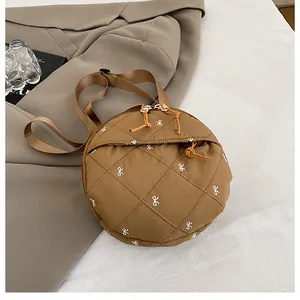 Detail of round quilted brown crossbody bag featuring white bow embroidery and zip puller