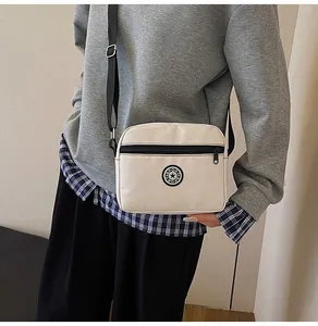 Crossbody view of a cream oxford cloth bag with adjustable black strap and sport logo