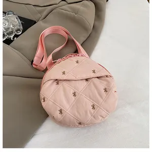 Detail of pink quilted round bag with gold bow embroidery and nylon strap