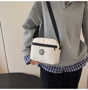 Detail of a beige nylon crossbody bag with 'SPORT' logo worn by a model in casual style