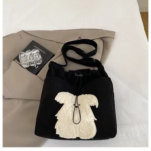 Close-up of black corduroy tote bag featuring a plush cartoon dog patch and drawstring