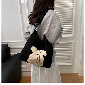 Detail of black corduroy tote bag with plush cartoon animal decor and drawstring closure