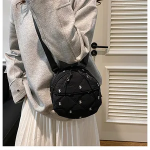 Detail of black quilted round bag featuring bow embroidery and adjustable shoulder strap