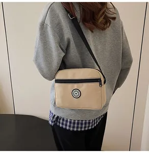 Detail view of the beige nylon crossbody bag with black zipper and sport logo