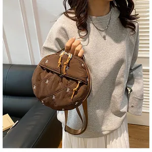 Detail of round quilted shoulder bag in dark brown with white bow embroidery