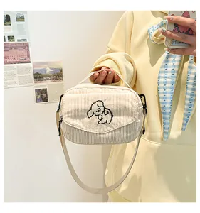 Detail van beige corduroy crossbodytas met schattig hondenborduurwerk en handvat