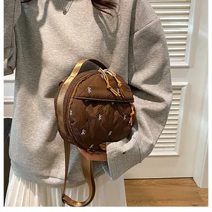 Detail of round quilted brown crossbody bag with white bow patterns and dual zippers