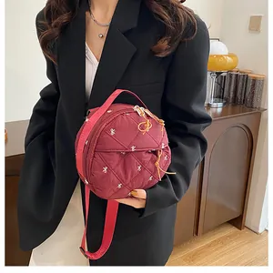 Close-up of burgundy quilted round bag with white bow embroidery and golden zipper details