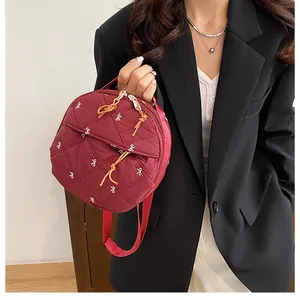 Detail of burgundy round quilted handbag with bow embroidery and corded zippers
