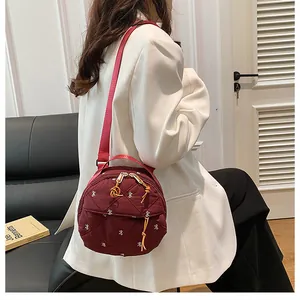 Detail view of burgundy quilted round shoulder bag with white bow embroidery on a model