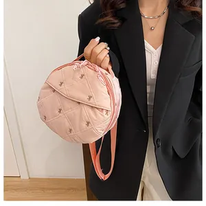 Detail of pink quilted round crossbody bag featuring elegant bow embroidery and texture