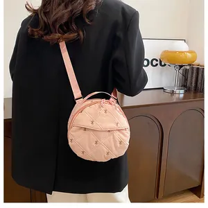 Detail of pink quilted nylon round crossbody bag with small embroidery and fabric strap