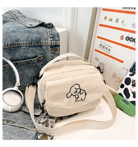 Detail van kleine crème corduroy schoudertas met schattig cartoon hondenborduurwerk erop