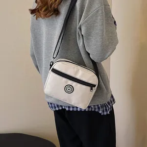 White nylon crossbody bag with Sport badge and black adjustable strap shown on model