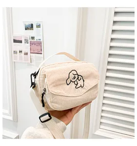 Detail van beige corduroy schoudertas met schattig geborduurd cartoon hondje