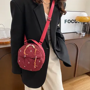 Quilted round crossbody bag in dark red with white bow print and woven shoulder strap