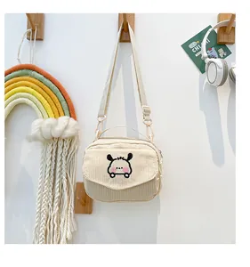 Détail du sac bandoulière en velours côtelé beige avec broderie cartoon sur un crochet