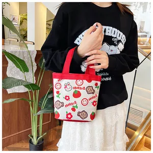 Detail der süßen Cartoon Canvas Handtasche mit roten Henkeln und Erdbeerdrucken in Hand