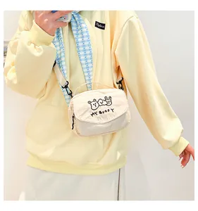 Detail van beige corduroy crossbody tas met schattig berenborduursel en stoffen schouderband