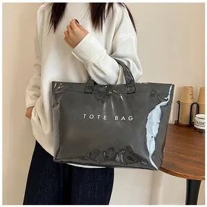 Dettaglio di una borsa tote in PVC nero lucido con scritta bianca TOTE BAG in uso