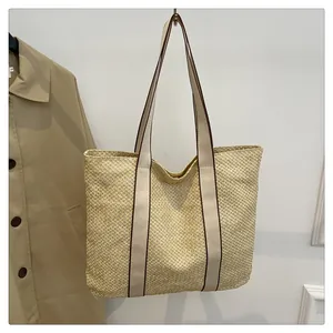 Detail der handgeflochtenen Strohtasche mit Kontrastnähten vor einem beigen Mantel