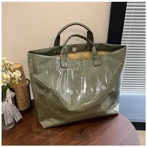 Dettaglio della borsa tote verde in Tyvek con testo bianco su tavolo con margherite