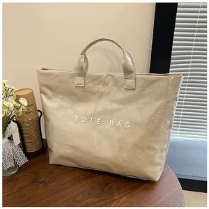 Dettaglio macro della borsa tote in PVC crema con trama lucida stropicciata e scritta TOTE BAG