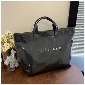 Dettaglio di una borsa tote in PVC nero lucido con scritta TOTE BAG su tavolo in legno